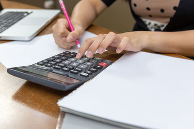 Midsection of woman using calculator on table