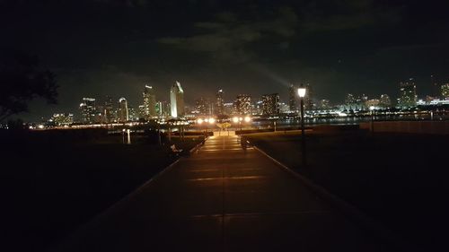 Illuminated street amidst buildings against sky at night