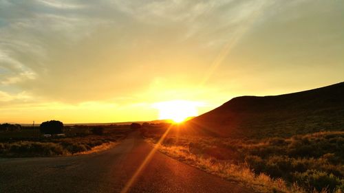 Road on field against sky during sunset