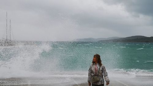 Woman standing against splashing water at beach against sky