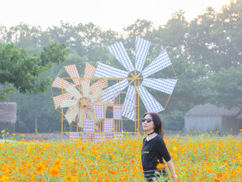 Portrait of young woman standing by flowers in field