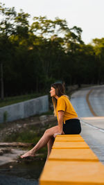 Woman sitting on yellow umbrella against plants