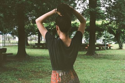 Rear view of woman tying hair on field