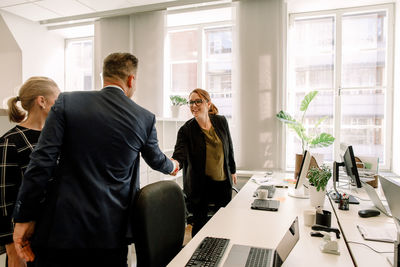 Businesswoman shaking hand with businessman while standing in office