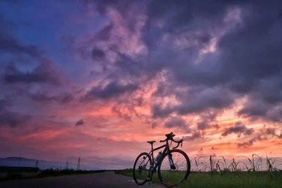 Bicycle on field against sky at sunset