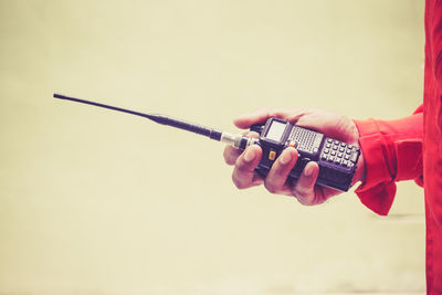 Midsection of man holding walkie-talkie while standing against wall