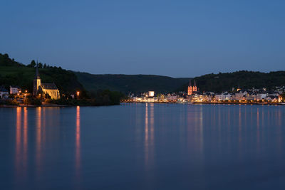 Illuminated buildings by sea against clear sky at night