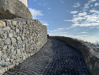 Stone wall by footpath against sky