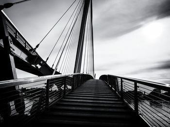 Footbridge by suspension bridge against sky