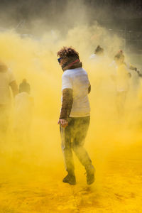 Full length of man woman standing in yellow powder paint dust during holi