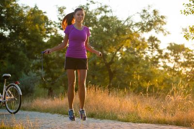Young woman skipping on road amidst trees during sunset