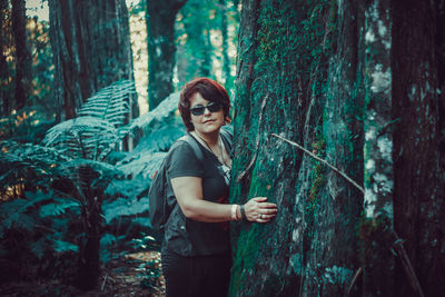 Woman standing by tree trunk in forest