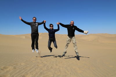 Full length of people on sand dune against clear sky