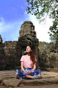 Young woman sitting on temple against sky