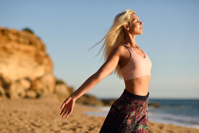 Side view of carefree young woman with eyes closed standing at beach