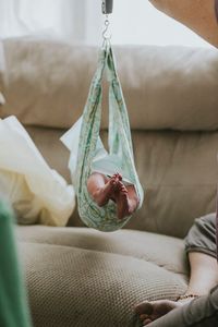 Low section of baby relaxing in hammock over sofa at home