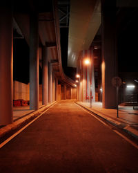 Empty road along illuminated bridge at night