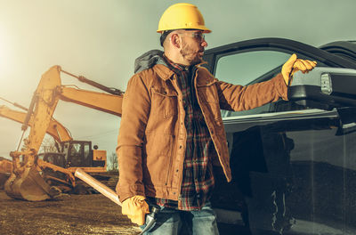 Man with hammer standing by car at site