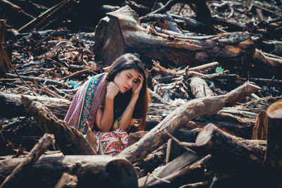 Full length of woman sitting on wood in forest