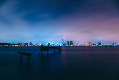 Illuminated city by river against sky at night