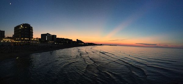 Scenic view of sea by buildings against sky during sunset