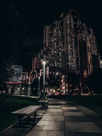 Illuminated street amidst buildings against sky at night