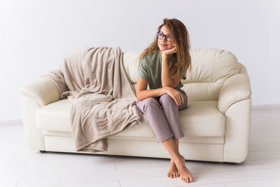 Full length of woman reading book sitting on sofa