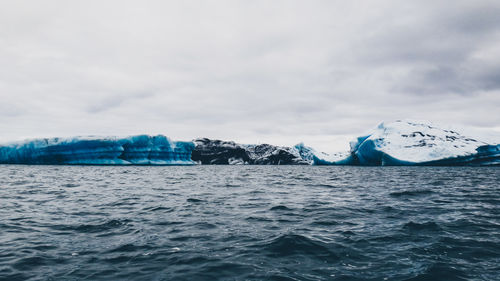 Icebergs in sea against cloudy sky