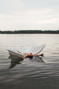 Shirtless woman floating with inflatable raft on lake against sky