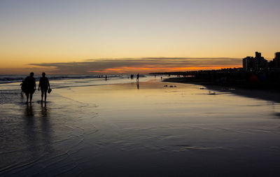 Silhouette people on beach against sky during sunset