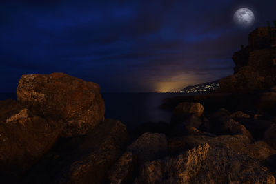 Rocks by sea against sky at sunset