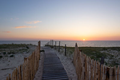 Walkway at beach against sky during sunset