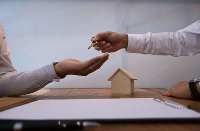 Cropped hand of man giving key to owner at desk in office