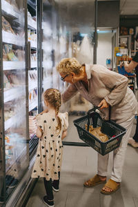 Girl buying frozen foods from refrigerated section with grandmother at grocery store