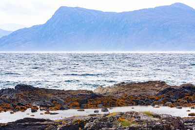 Scenic view of sea by mountains against sky