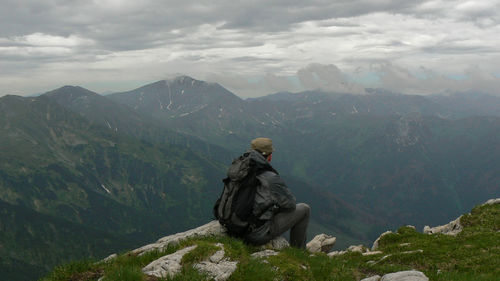 Man sitting on mountain against sky