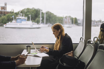 Side view of businesswoman using laptop while sitting at table in ferry