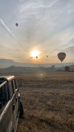 Hot air balloons on field against sky during sunset