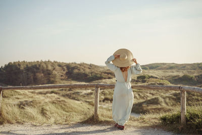 Rear view of woman standing on field against sky