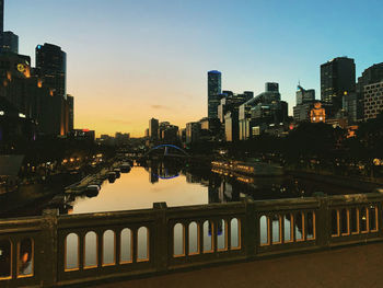 Illuminated buildings by river against sky in city