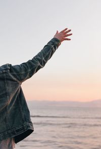 Midsection of person with arms raised by sea against sky