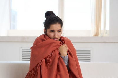 Sick woman wearing blanket sitting at home
