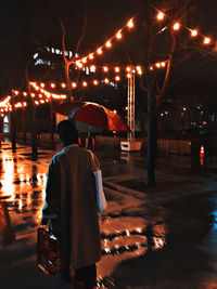 Rear view of man standing on illuminated street at night