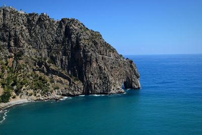 Scenic view of sea by cliff against clear blue sky