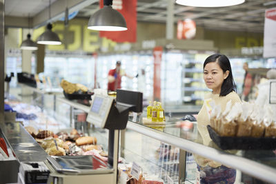 Female customer standing in front of deli counter in supermarket and checking products