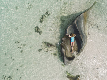 Drone shot of woman relaxing on rock at beach