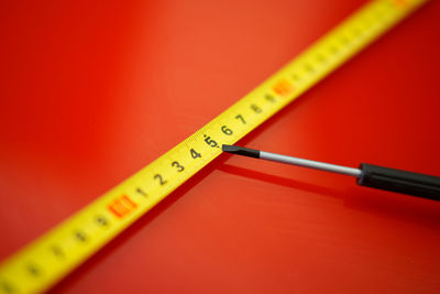 Close-up of screwdriver and measuring tape over red background