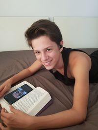 Portrait of smiling boy with book while lying on bed at home