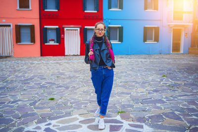 Full length portrait of smiling young woman standing against building