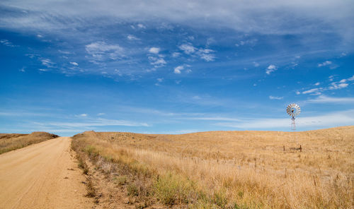 Dirt road amidst field against sky